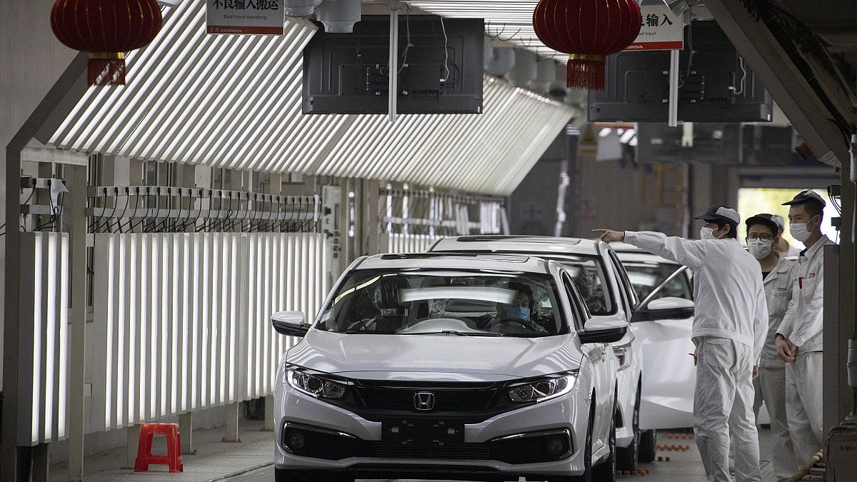 In this April 8, 2020, photo, workers wearing masks against the coronavirus chat near finished cars rolled out at the Dongfeng Honda Automobile Co., Ltd factory in Wuhan.
