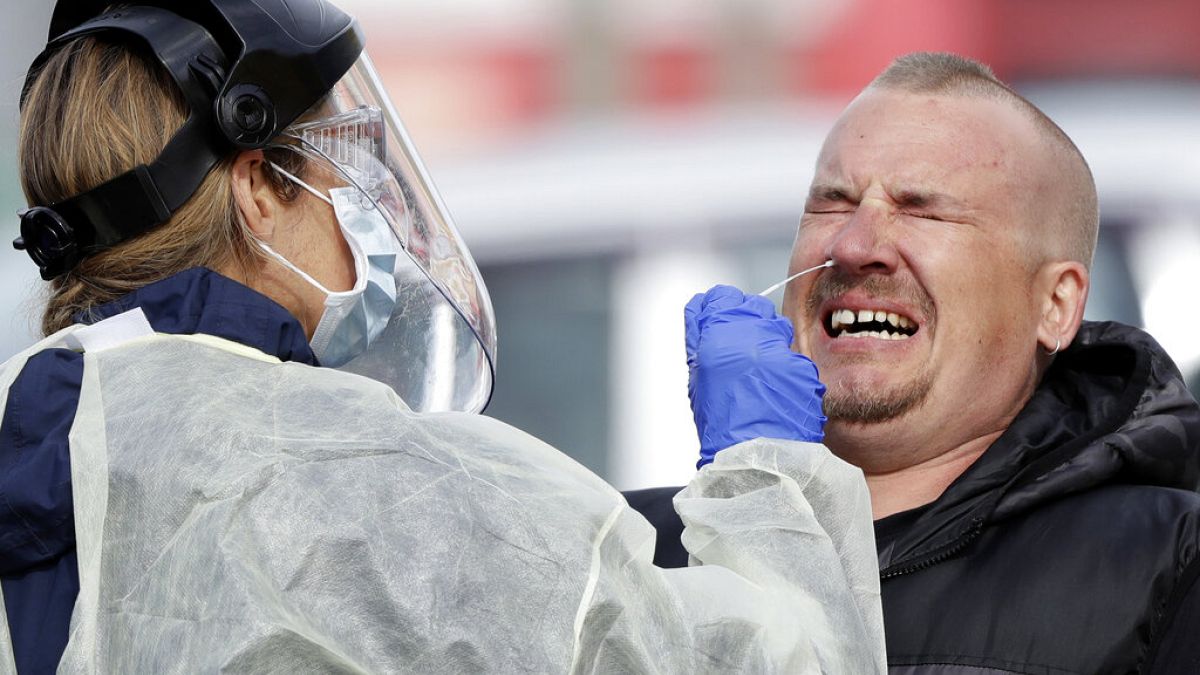 A man reacts as a medical staffer tests shoppers who volunteered at a pop-up community COVID-19 testing station at a supermarket car park in Christchurch, New Zealand