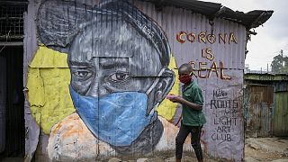 A boy wearing a face mask as he walks past an informational mural warning people about the risk of the new coronavirus, painted by artists from the Mathare Roots youth group
