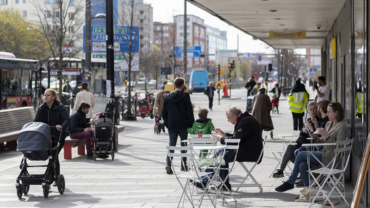 Des gens mangent des glaces dans un café en plein air alors que d'autres passent dans le centre de Stockholm, en Suède, le lundi 20 avril 2020.