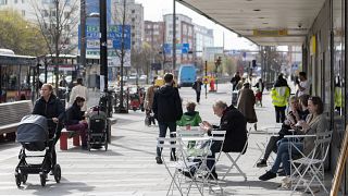 Des gens mangent des glaces dans un café en plein air alors que d'autres passent dans le centre de Stockholm, en Suède, le lundi 20 avril 2020.