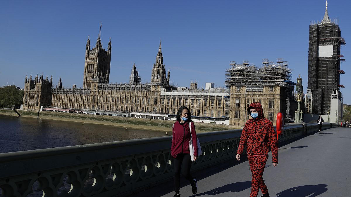 People wear masks as they walk near Britain's Houses of Parliament as it goes back to work, London, Tuesday, April 21, 2020. 