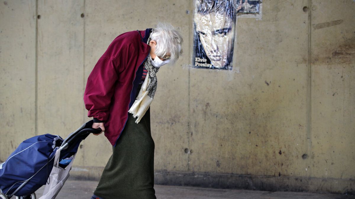 An elderly woman drags a shopping trolley, backdropped by an Elvis Presley poster, at a market place in Bucharest, Romania