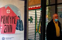 A pedestrian wearing a mask passes an advertisment at a bus stop that reads "Stay Home, Hellenic Republic-Health Ministry" in Athens, Wednesday, March 18, 2020