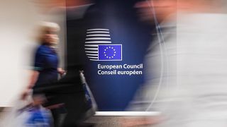 People walk by a sign in English and French in the press room at an EU summit in Brussels on Tuesday, June 28, 2016. 