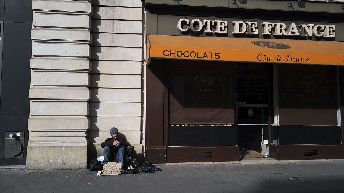 Бездомный сидит у закрытой кондитерской в Париже. 