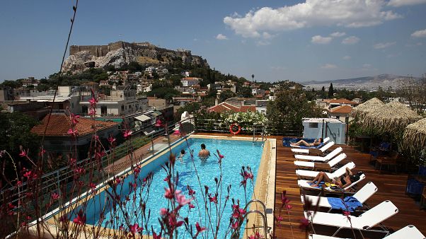 Tourists swim in a swimming pool on the roof of a hotel as the ancient Acropolis hill Tourists swim in a swimming pool on the roof of a hotel as the ancient Acropolis hill