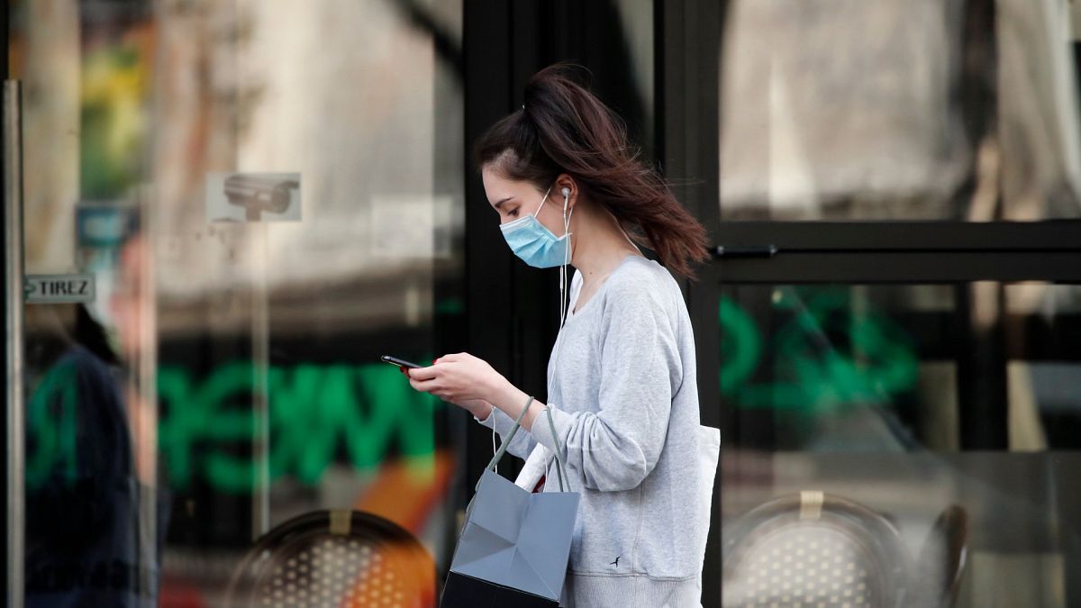 A woman wearing protective face mask walks looking at her phone past a closed restaurant during a nationwide confinement to counter the COVID-19, in Paris, April 20, 2020.