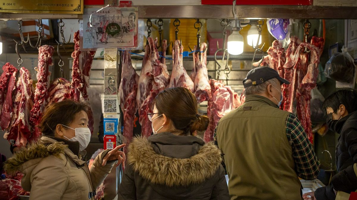 People wear face masks as they shop for meat at a market in Beijing, Saturday, March 14, 2020