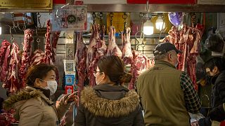 People wear face masks as they shop for meat at a market in Beijing, Saturday, March 14, 2020