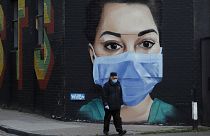 A man wearing a face mask and gloves to protect from coronavirus walks past a recently painted mural by professional street artist David Speed and the Graffiti Life collective