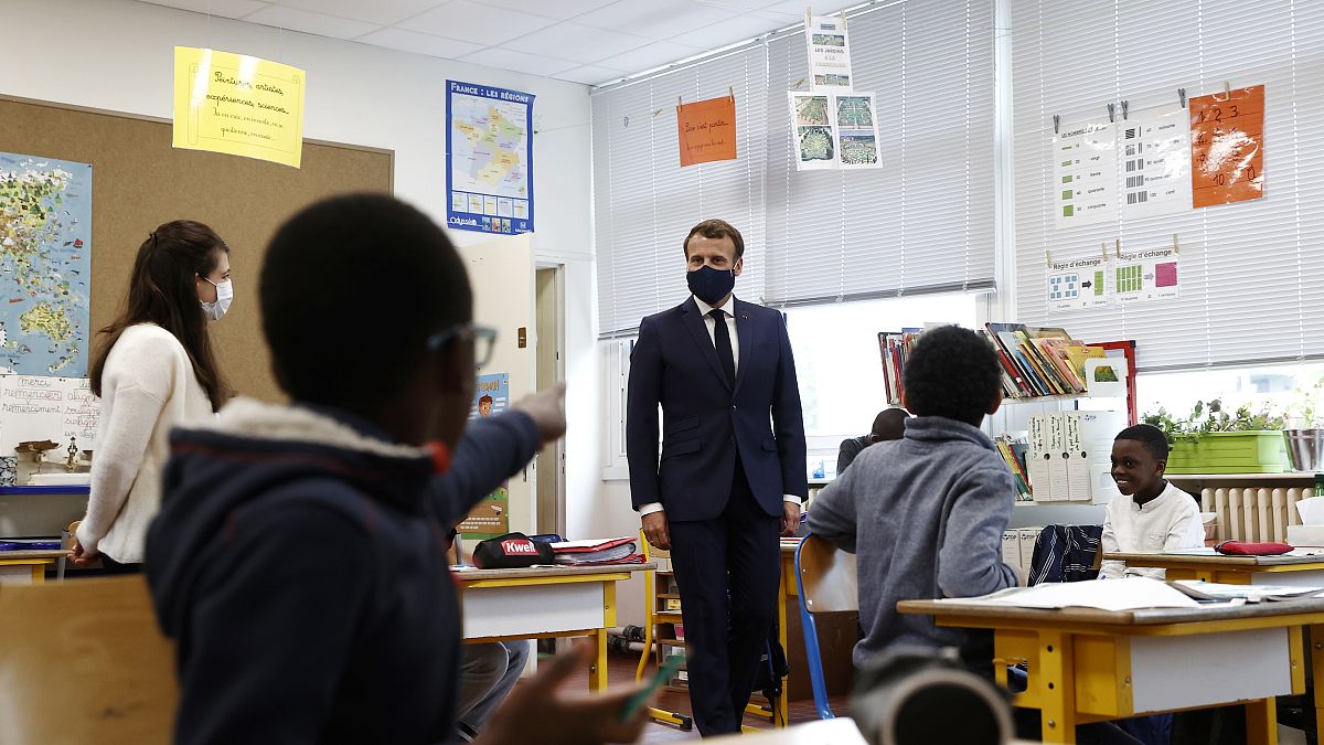 French President Emmanuel Macron wearing a protective mask with a blue-white-red colored ribbon listens to pupils during a visit elementary school in Poissy,