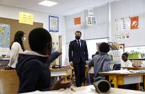 French President Emmanuel Macron wearing a protective mask with a blue-white-red colored ribbon listens to pupils during a visit elementary school in Poissy,