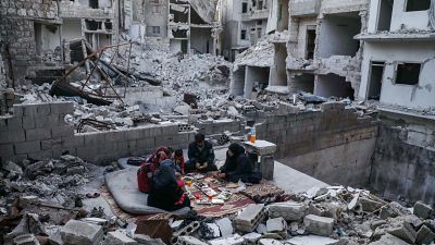 Members of a displaced Syrian family breaking their fast together for the sunset "iftar" meal, in the midst of the rubble of their destroyed home.