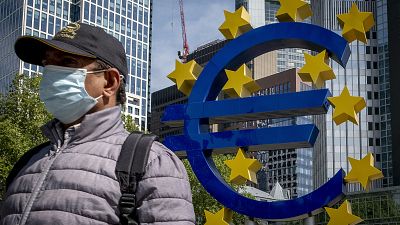 A man walks by the Euro sculpture in front of the old the European Central Bank in Frankfurt, Germany, Tuesday, May 5, 2020.