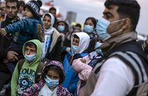 Refugees and migrants wearing masks to prevent the spread of the coronavirus, wait to get on a bus after their arrival at the port of Piraeus, near Athens