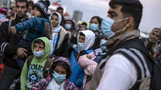 Refugees and migrants wearing masks to prevent the spread of the coronavirus, wait to get on a bus after their arrival at the port of Piraeus, near Athens