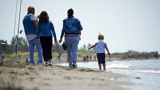 People walk along the beach of Ladispoli, a coastal town some 30 kilometers (18 miles) north of Rome, Saturday, May 9, 2020. 