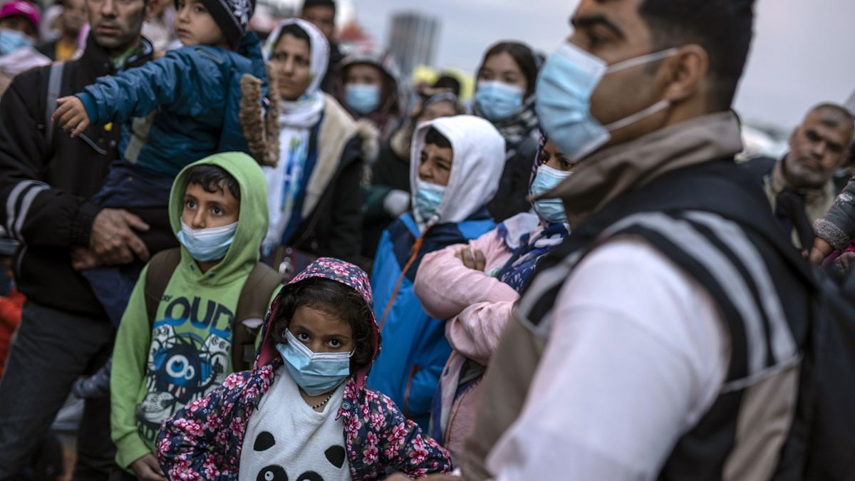 Refugees and migrants wearing masks to prevent the spread of the coronavirus, wait to get on a bus after their arrival at the port of Piraeus, near Athens on May 4, 2020.