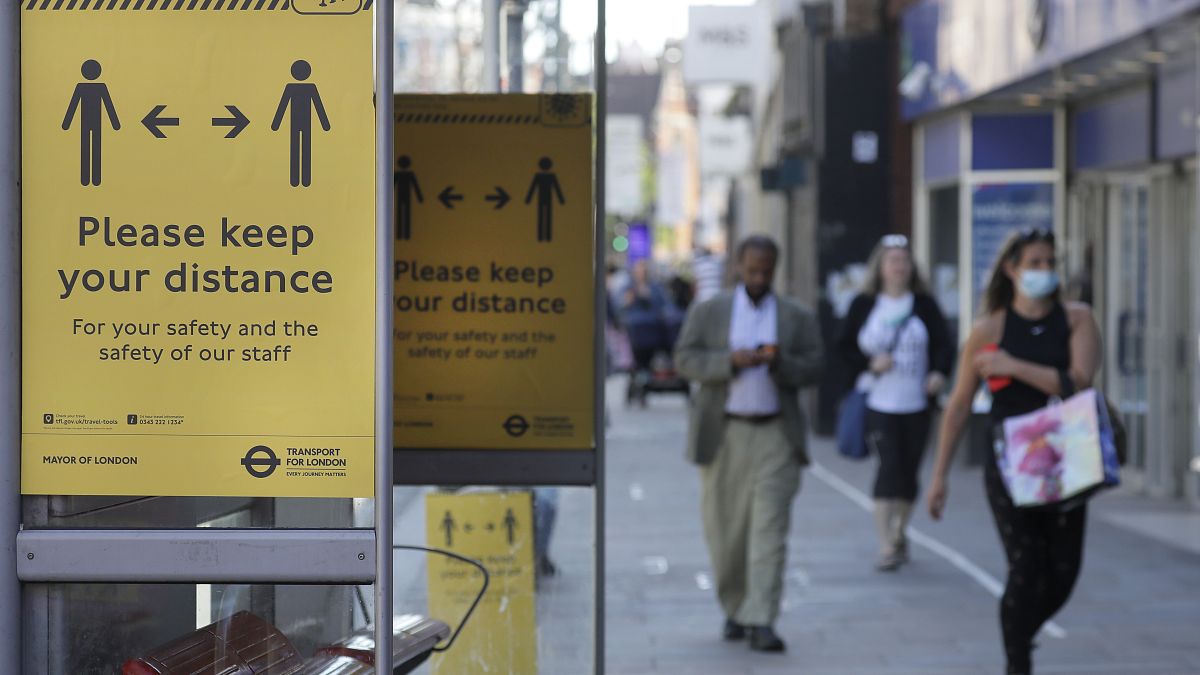 Signs advise people to social distance on a bus stop along a high street, in London
