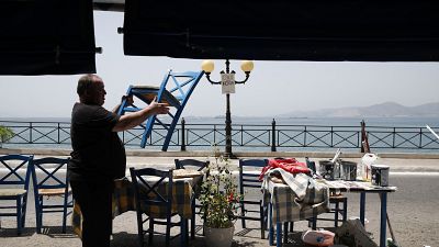 Un trabajador coloca sillas en un restaurante de pescado antes de su reapertura en el Pireo.