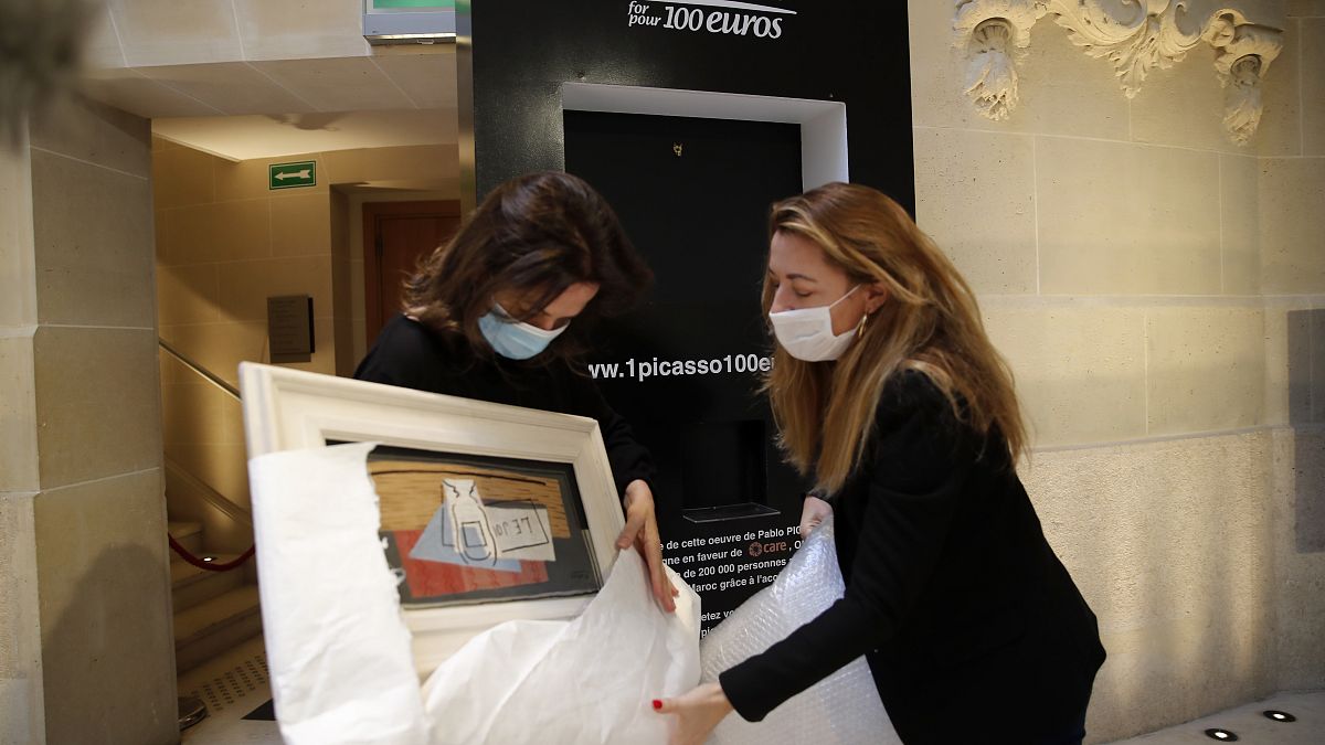 Raffle organizers Peri Cochin, left, and Arabenne Reille unbox the painting "Nature morte" by Picasso at Christie's auction house, Tuesday, May 19, 2020 in Paris