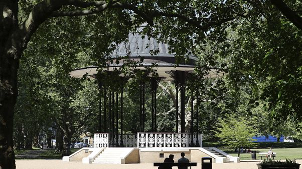 People sit on benches near the bandstand in Southwark Park in London, Tuesday, May 19, 2020 People sit on benches near the bandstand in Southwark Park in London, Tuesday, May 19, 2020