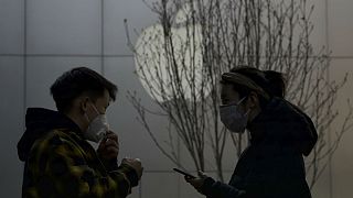 Masked shoppers stand near the Apple logo in Beijing