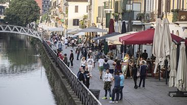People walk along the Naviglio grande canal in Milan, Italy, Monday, May 18, 2020