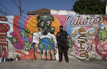 Graffiti artist Angelo Campos poses for a photo by his mural referencing the COVID-19 pandemic which he said he painted in honor of health workers in Rio de Janeiro, Brazil