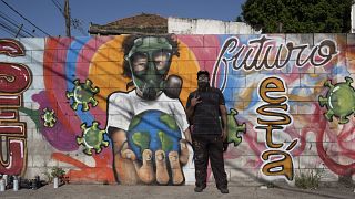 Graffiti artist Angelo Campos poses for a photo by his mural referencing the COVID-19 pandemic which he said he painted in honor of health workers in Rio de Janeiro, Brazil