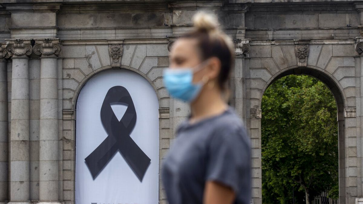 A woman wearing a face mask to protect against coronavirus, walks in front of a black ribbon for the victims of COVID-19, displayed at Puerta de Alcala square in downtown Madr