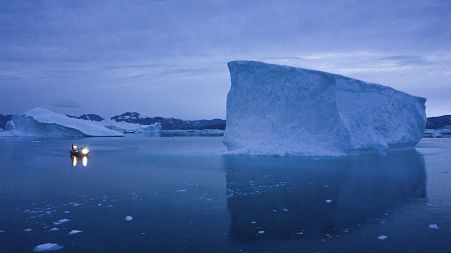 A boat navigates at night next to large icebergs in eastern Greenland.