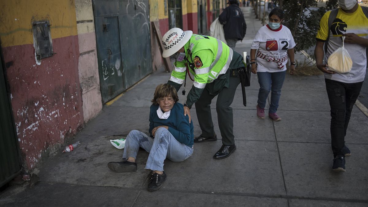 Un policía ayuda a una mujer tendida en una calle de Lima, Perú