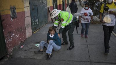 Un policía ayuda a una mujer tendida en una calle de Lima, Perú
