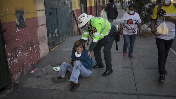 Un policía ayuda a una mujer tendida en una calle de Lima, Perú Un policía ayuda a una mujer tendida en una calle de Lima, Perú