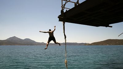 A boy dives into the sea from an old dock on the Aegean Sea island of Milos, Greece, Sunday, May 24, 2020.