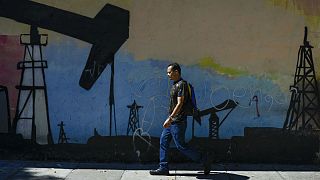 A man walks past a mural featuring oil pumps and wells in Caracas, Venezuela