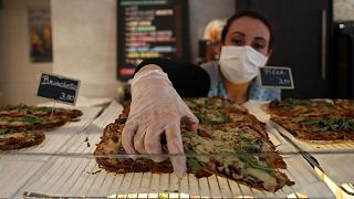 A baker woman wearing gloves and protective mask serves a bruschetta, in Paris