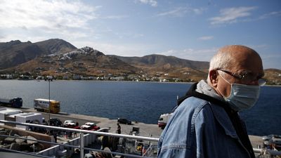 A passenger wearing a face mask to prevent the spread of the new coronavirus, stands on the deck of a ferry as it approaches the Aegean Sea island of Serifos