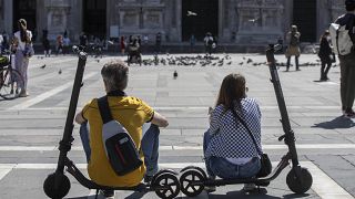 A woman and a man relax sitting on their scooters at the Duomo square, in Milan, Italy, Monday, May 25, 2020.