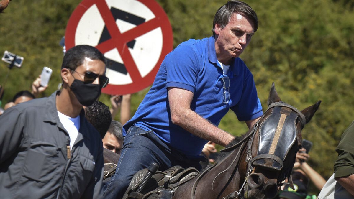 Brazil's President Jair Bolsonaro rides a horse greeting supporters outside the presidential palace in Brasilia, Brazil, Sunday, May 31, 2020. (AP Photo/Andre Borges)