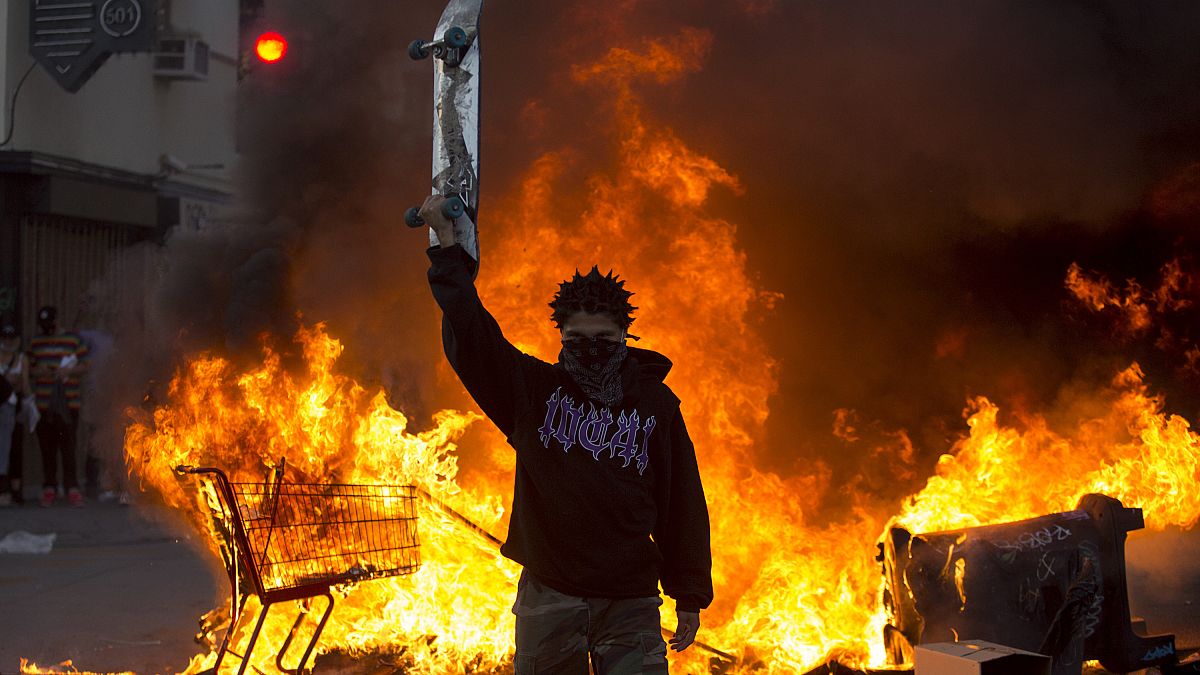 A protester holds a skateboard in front of a fire in Los Angeles