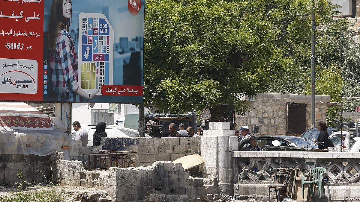 أناس يمشون في دمشق قرب لوحة إشهارية لأكبر مشغل للهواتف المحمولة في البلاد يملكها رامي مخلوف - 2020/05/11