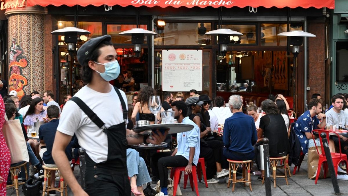 A waiter wearing a face mask serves clients while people eat and have drinks on the terrace of the cafe-restaurant "Le Bar du Marche" in Paris on June 2, 2020