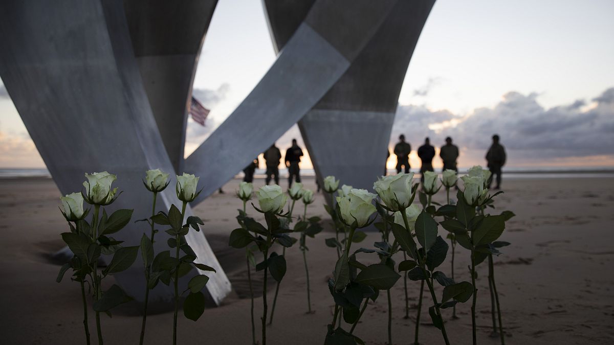 Men in a vintage US WWII uniforms stand behind flowers left at Les Braves monument after a D-Day 76th anniversary ceremony in Saint Laurent sur Mer, Normandy, France, Saturday