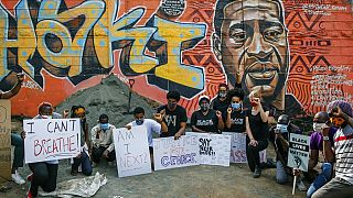Protesters against police violence gather next to a new mural painted this week showing George Floyd with the Swahili word "Haki" meaning "Justice".