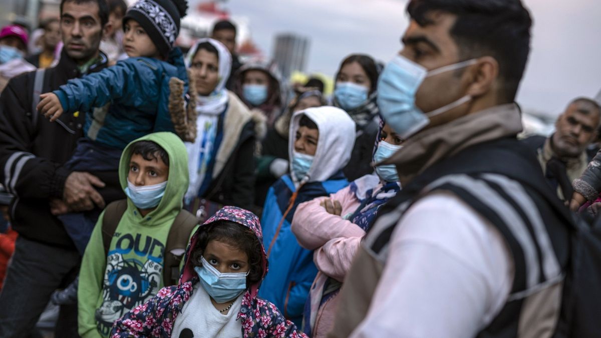 Refugees and migrants wearing masks to prevent the spread of the coronavirus, wait to get on a bus after their arrival at the Greek port of Piraeus