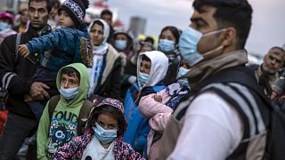 Refugees and migrants wearing masks to prevent the spread of the coronavirus, wait to get on a bus after their arrival at the Greek port of Piraeus