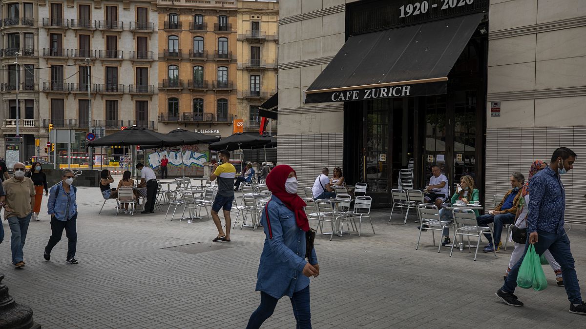 In this Monday, June 1, 2020 photo, people walk past a terrace bar with local customers in Barcelona downtown.